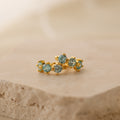 The Triple Aquamarine Huggies feature clusters of light blue gemstones on gold hoops, displayed atop a beige stone—perfect minimalist earrings customizable with birthstones.