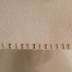 A row of petite gemstone earrings, including Garnet Drop Studs, displayed on a beige textured fabric background.