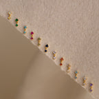 Topaz Drop Studs with colorful gemstones arranged in a row on a textured beige surface make a vibrant accessory for any occasion.