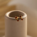 Garnet Drop Studs, featuring three vivid red gemstones, are displayed on a smooth beige cylindrical stand, evoking the elegance of birthstone jewelry.