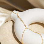 Diamond Bezel Hand Chain in 18K Gold featuring round gemstones, elegantly draped over a smooth white ceramic donut-shaped object.