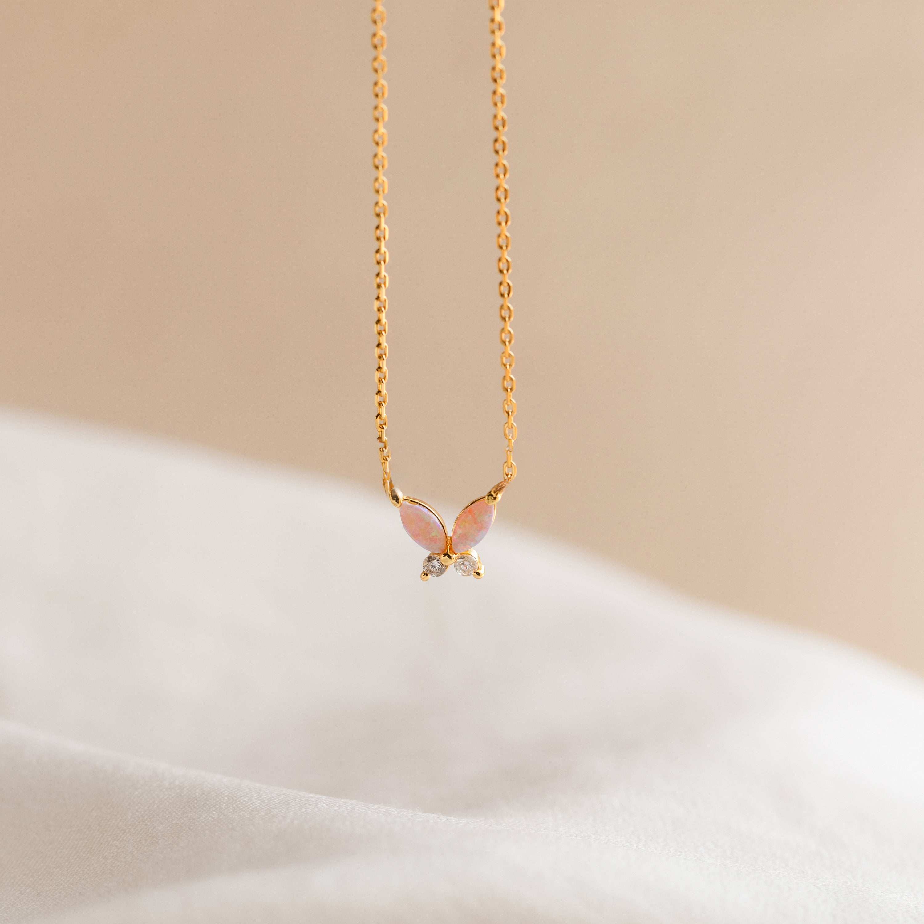 Pink Opal Butterfly Necklace in 18K Gold, featuring a delicate butterfly charm, photographed on a soft beige and white background.