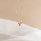 The Pink Opal Butterfly Necklace showcases a delicate butterfly pendant on gold, photographed against a soft beige background—a charming gemstone necklace for any occasion.