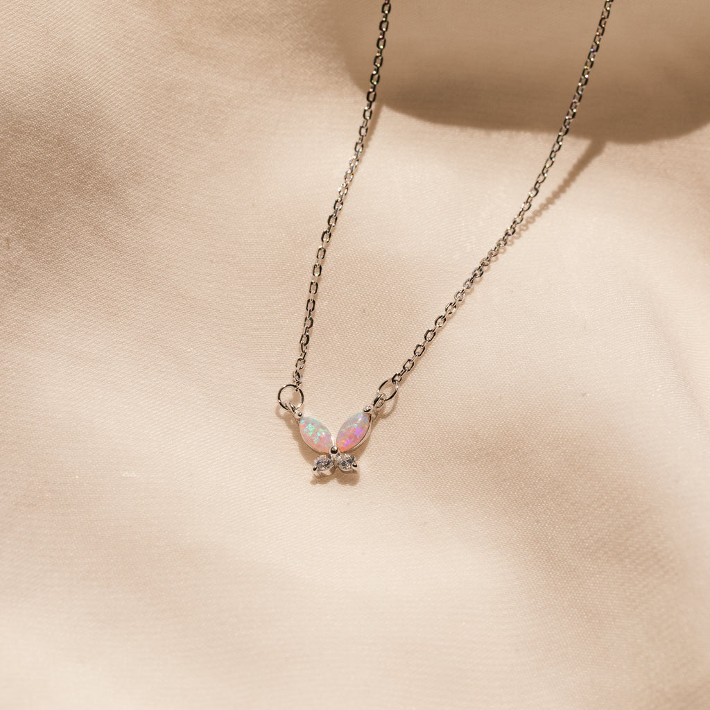 Pink Opal Butterfly Necklace displayed on a soft beige fabric background.