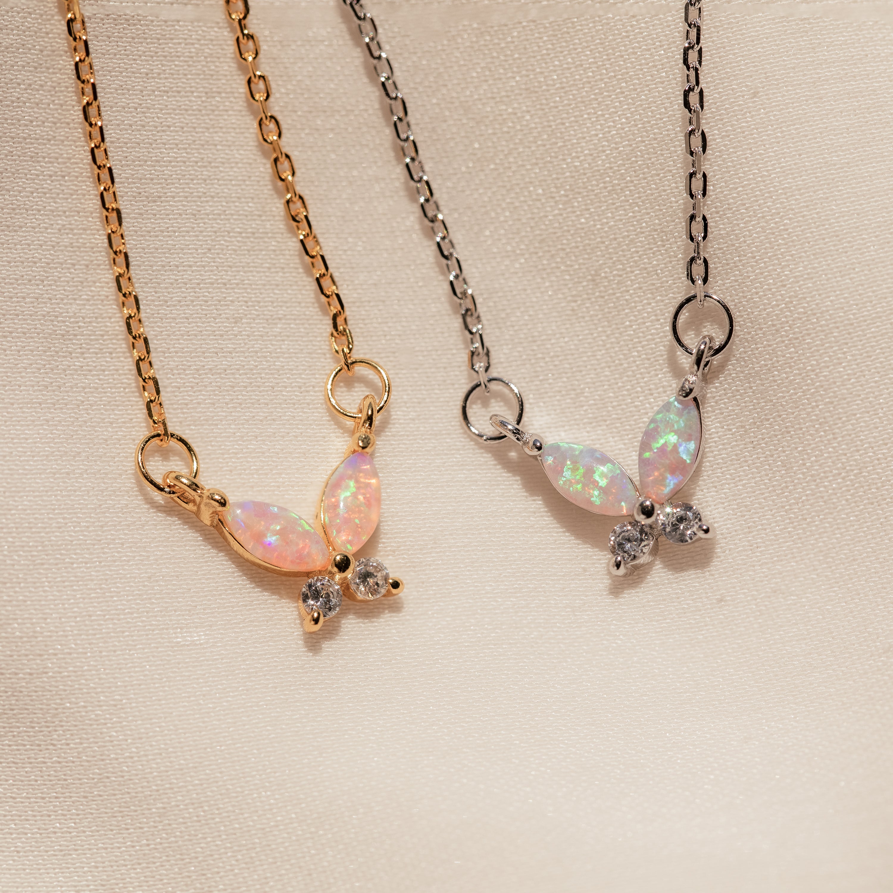 A Pink Opal Butterfly Necklace in Silver rests on a light fabric background, its butterfly-shaped pendant hanging from a delicate silver chain.