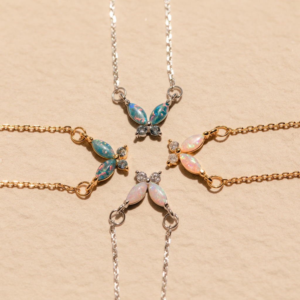 Four butterfly-shaped gemstone bracelets in gold and silver are arranged in a circle on beige, perfectly complementing the Pink Opal Butterfly Necklace.