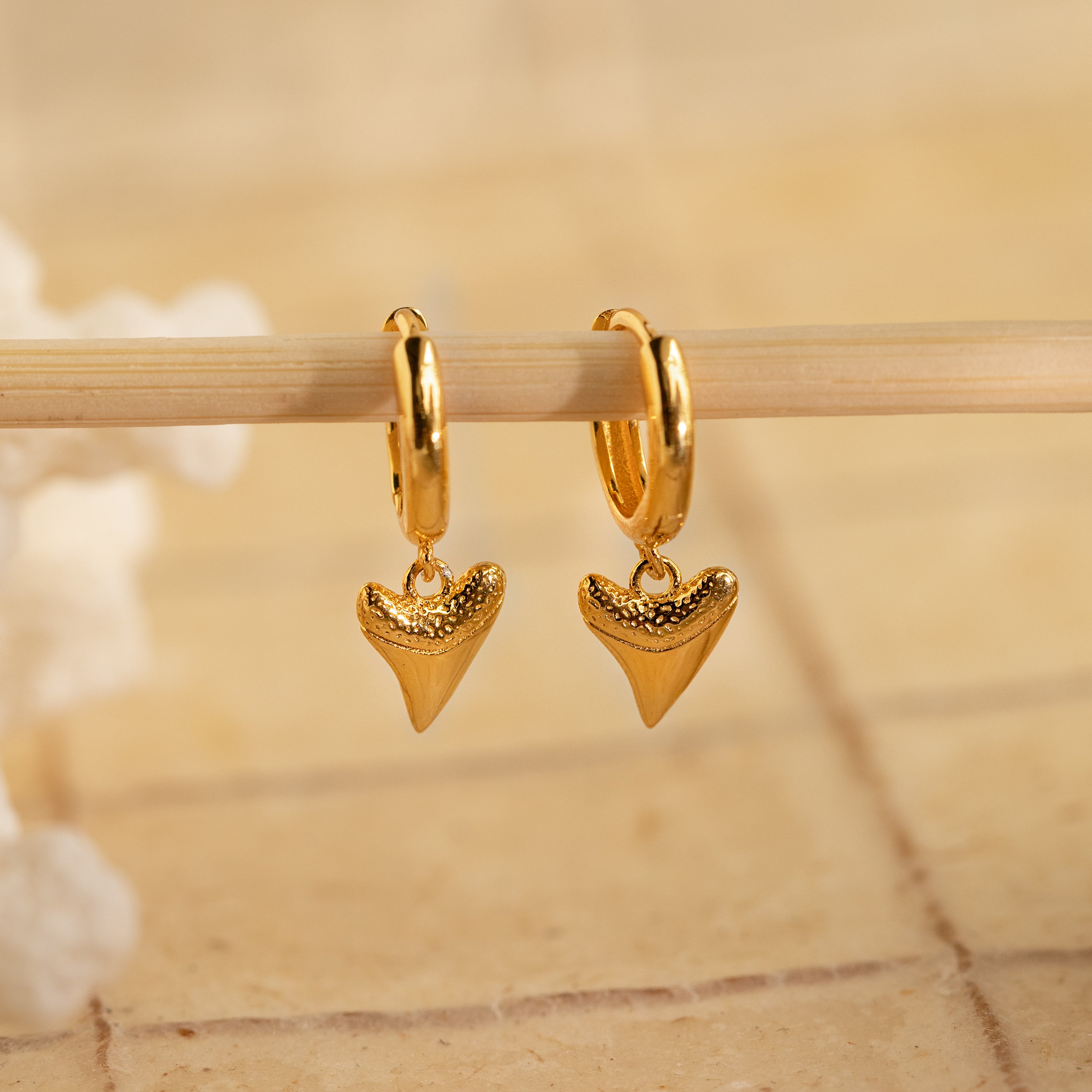 Add edge to your beach look with Shark Tooth Huggies—gold hoop earrings featuring shark tooth-shaped pendants. Bold and stylish, they stand out against any neutral backdrop.