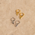Two pairs of Shark Tooth Huggies—one gold, one silver—rest on a beige surface, making them the perfect bold accessories for your next beach vacation.