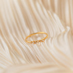 The Delicate Pearl Diamond Ring, accented with small diamonds, is displayed on soft, cream-colored fabric.