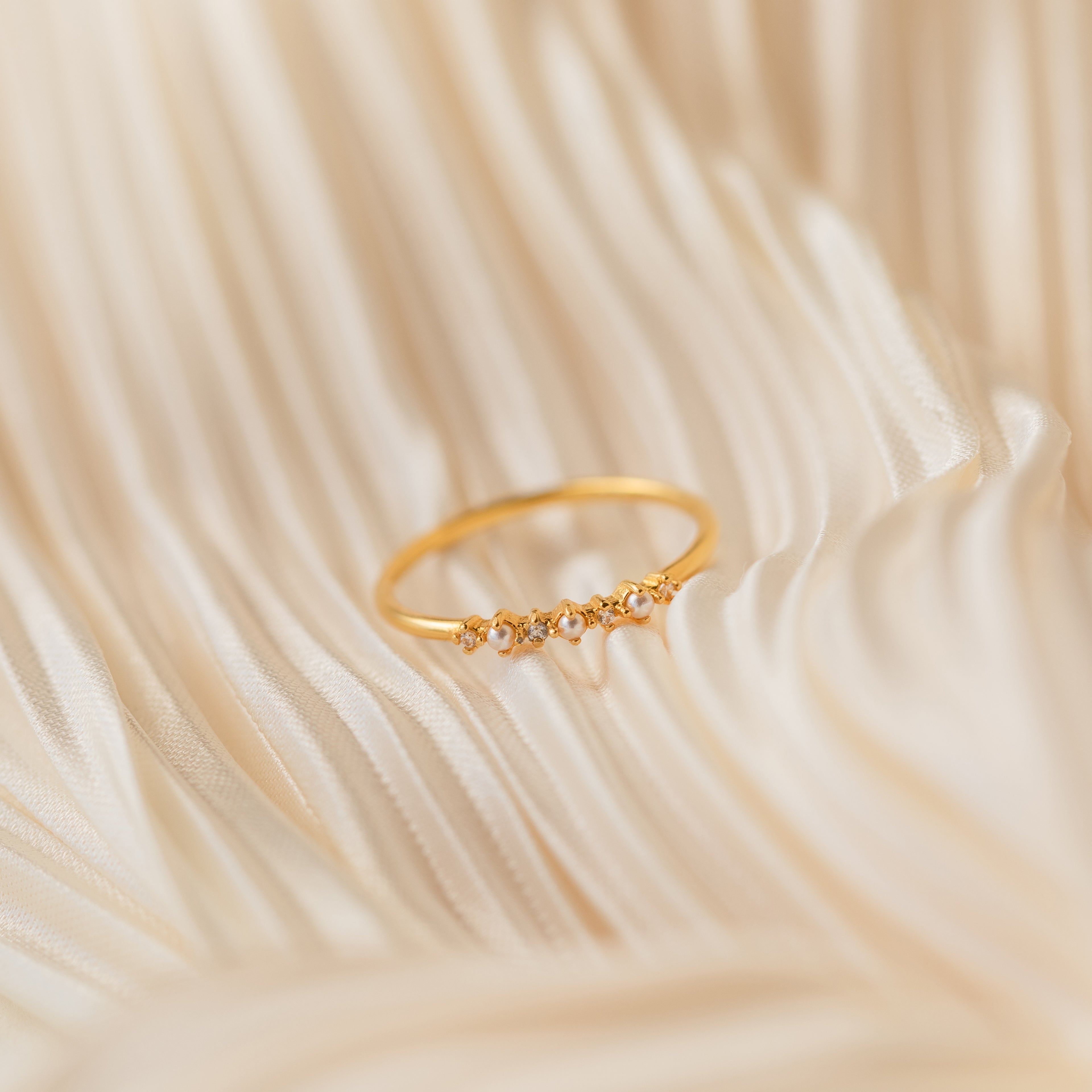 The Delicate Pearl Diamond Ring, accented with small diamonds, is displayed on soft, cream-colored fabric.