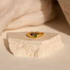 The Signet Mood Ring features a color-changing green gemstone on a textured white stone, set against a soft beige background—nostalgic jewelry with a modern twist.