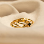 The Black Abyss Ring Set features three gold dainty bands with black gemstones and small diamonds, displayed on a soft beige fabric background.