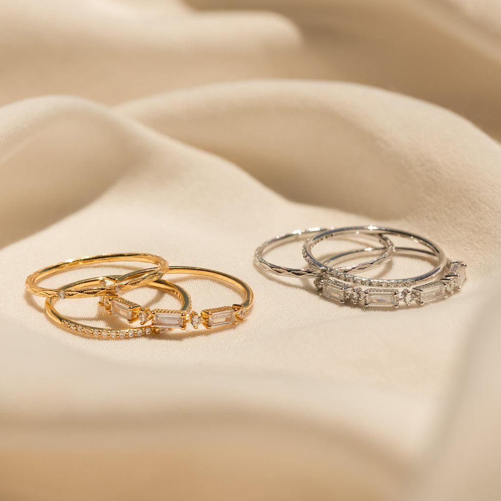 The Diamond Stacking Ring Set, featuring gold and silver bands with gemstones, is elegantly displayed on soft beige fabric—making it the perfect Christmas gift.