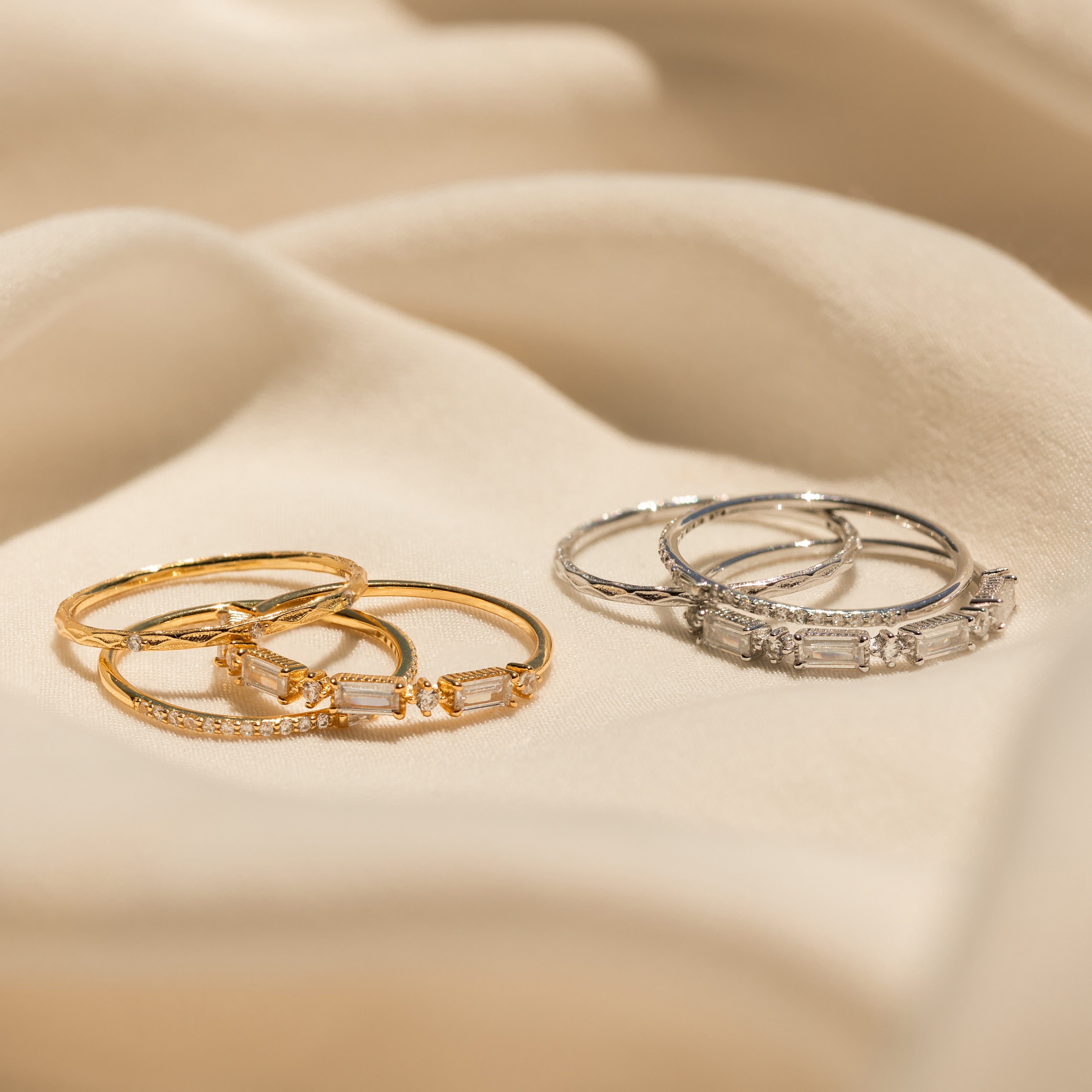 The Diamond Stacking Ring Set, featuring gold and silver bands with gemstones, is elegantly displayed on soft beige fabric—making it the perfect Christmas gift.