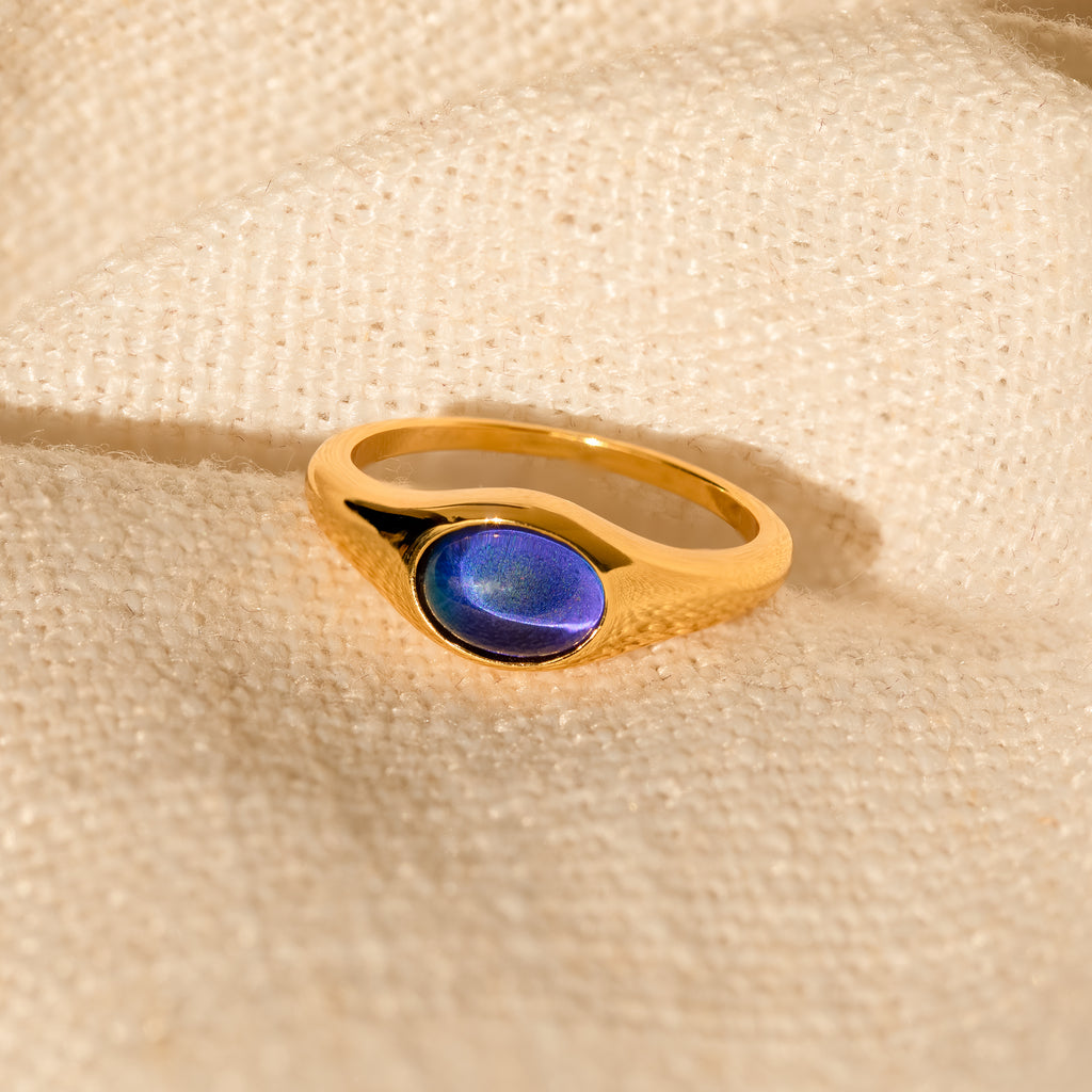 The Signet Mood Rings Set features gold signet rings with oval blue stones on soft beige fabric, blending nostalgic jewelry charm and modern color-changing appeal.