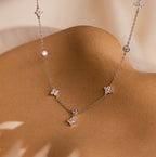 The Ivy Diamond Station Necklace in Silver features star-shaped and round diamond accents, elegantly displayed on a smooth tan surface.