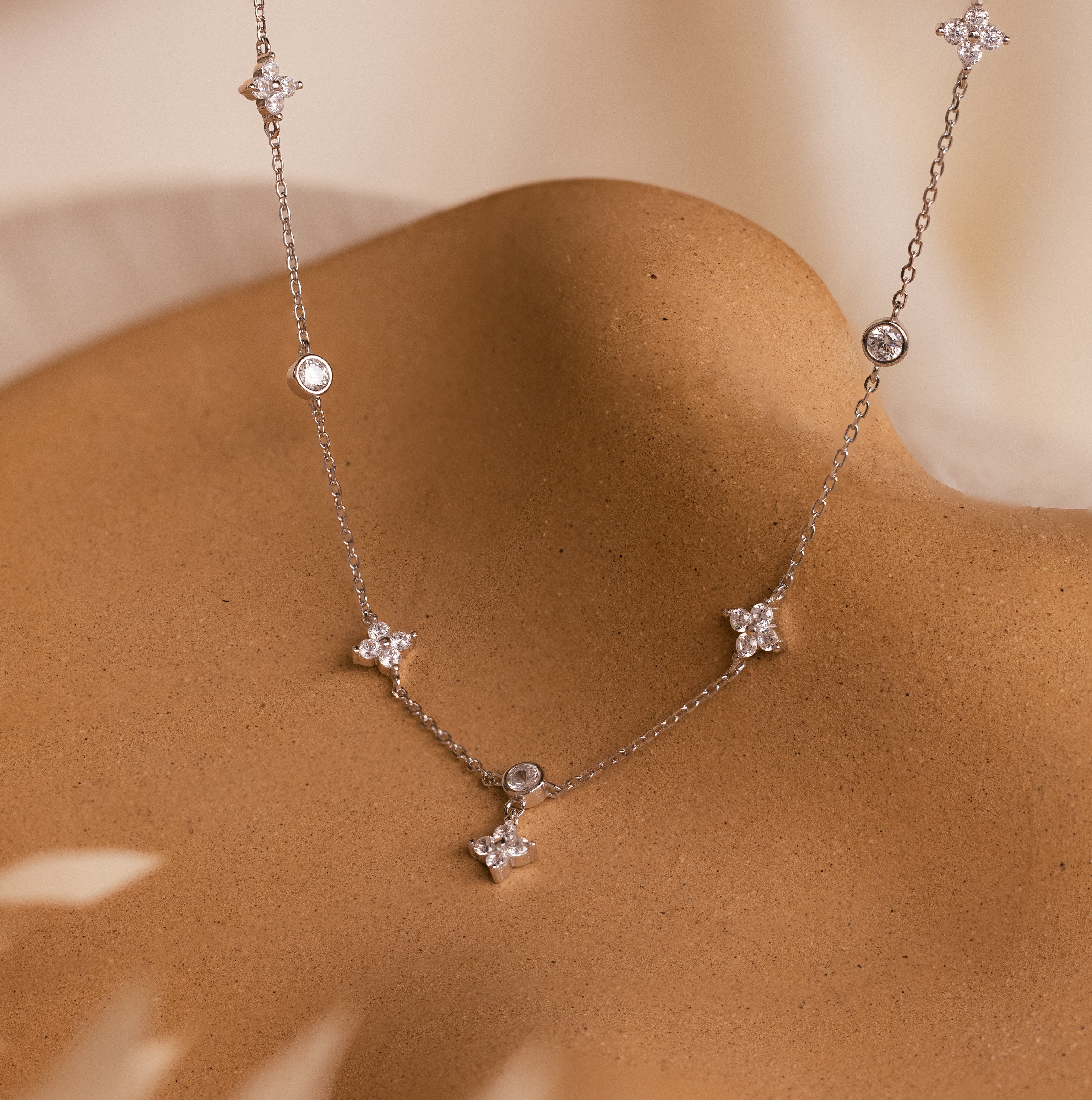 The Ivy Diamond Station Necklace in Silver features star-shaped and round diamond accents, elegantly displayed on a smooth tan surface.