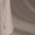 The Pearl Diamond Drop Necklace in Silver features a small pearl and diamond pendant, casting a delicate shadow on beige—ideal bridal jewelry.