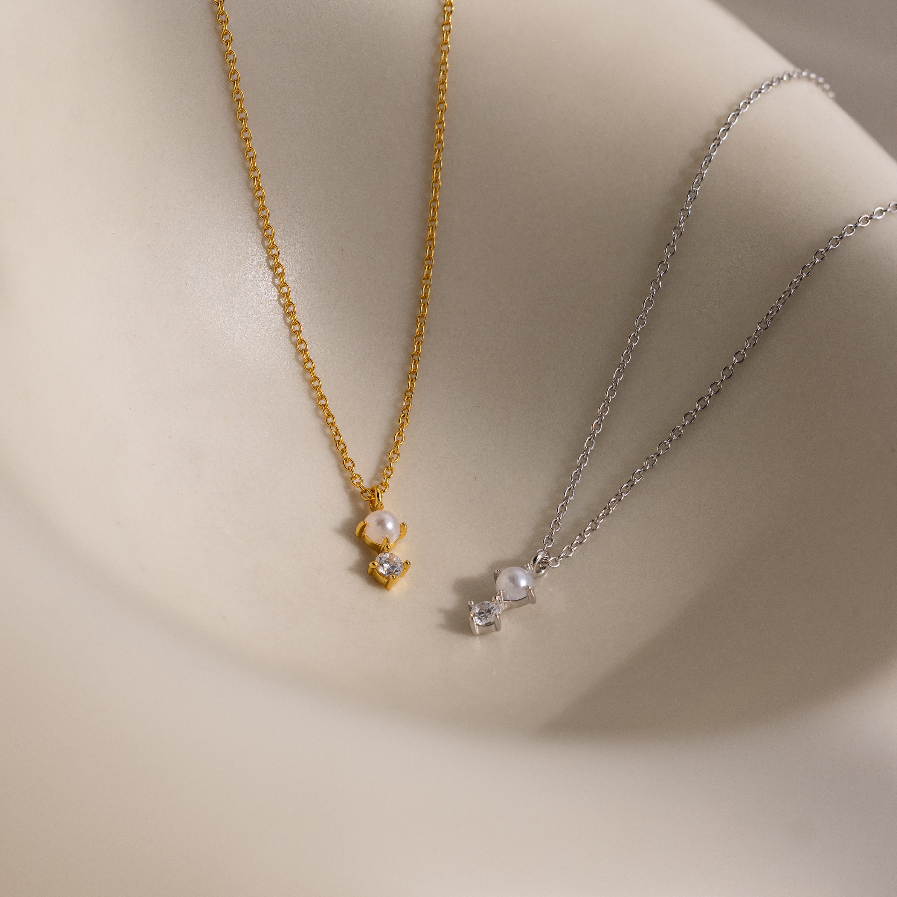 The Pearl Diamond Drop Necklace in Silver features a delicate pearl and sparkling gemstone, making it an elegant choice for bridal jewelry or as a stunning drop necklace displayed on any smooth surface.