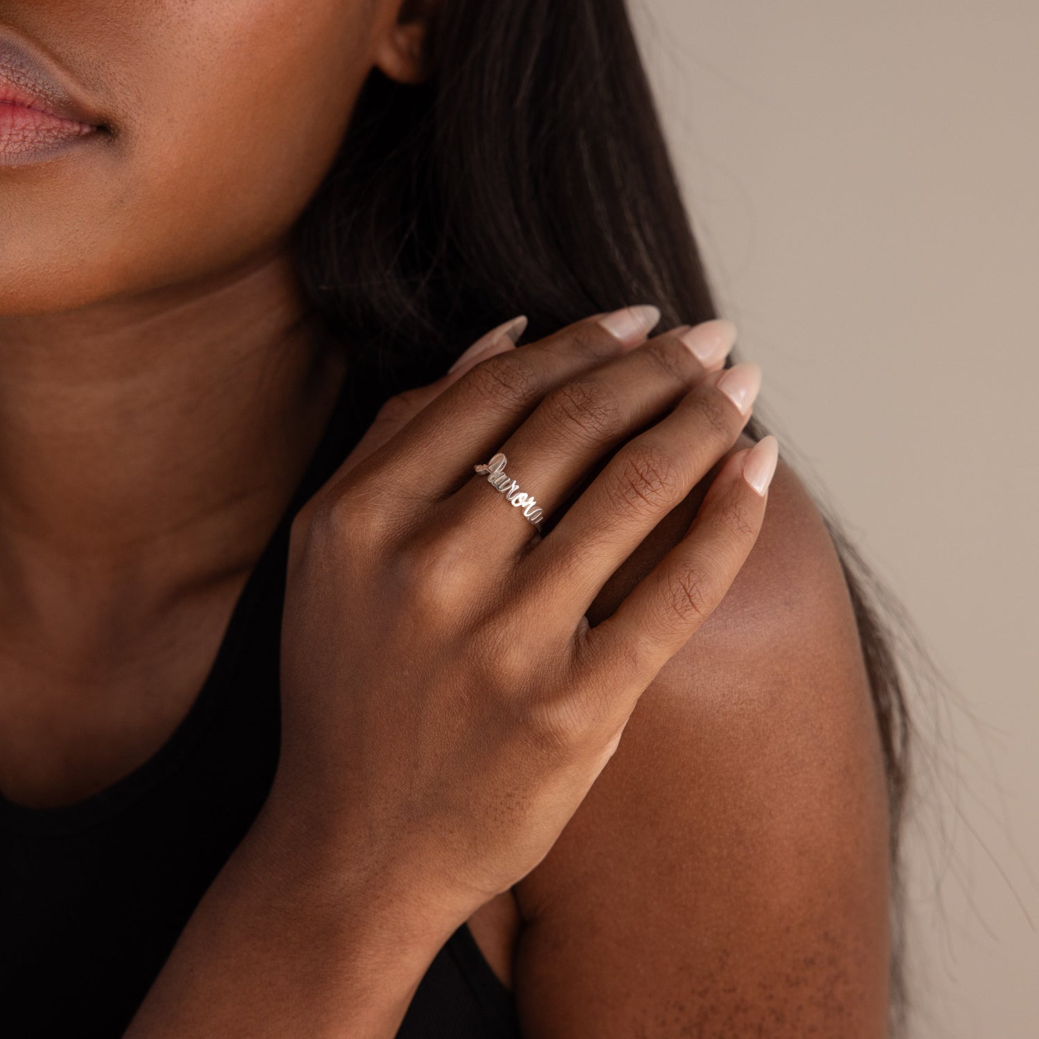 A woman with manicured nails gently touches her face while wearing the Grace Script Name Ring in Sterling Silver on her finger.