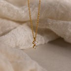The Pearl Diamond Drop Necklace features a petite pearl and diamond pendant—an elegant bridal jewelry piece displayed on soft, cream-colored fabric.