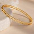 Lace Diamond Bangle in 18K Gold with small round diamonds and an open station design, shown on a light beige surface and white stone.