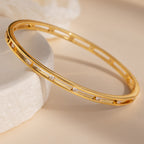 The Lace Diamond Bangle, featuring delicate gold and sparkling diamonds, is elegantly displayed on a light surface with soft, neutral lighting—a striking luxury jewelry piece.