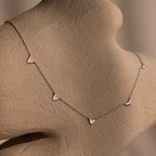 Heart Station Necklace in Silver, featuring delicate heart charms on a cable chain, displayed on a beige textured mannequin bust.