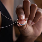 A hand holds the Inner Circle Necklace in Sterling Silver, featuring a sleek ring pendant gracefully suspended on a fine chain.