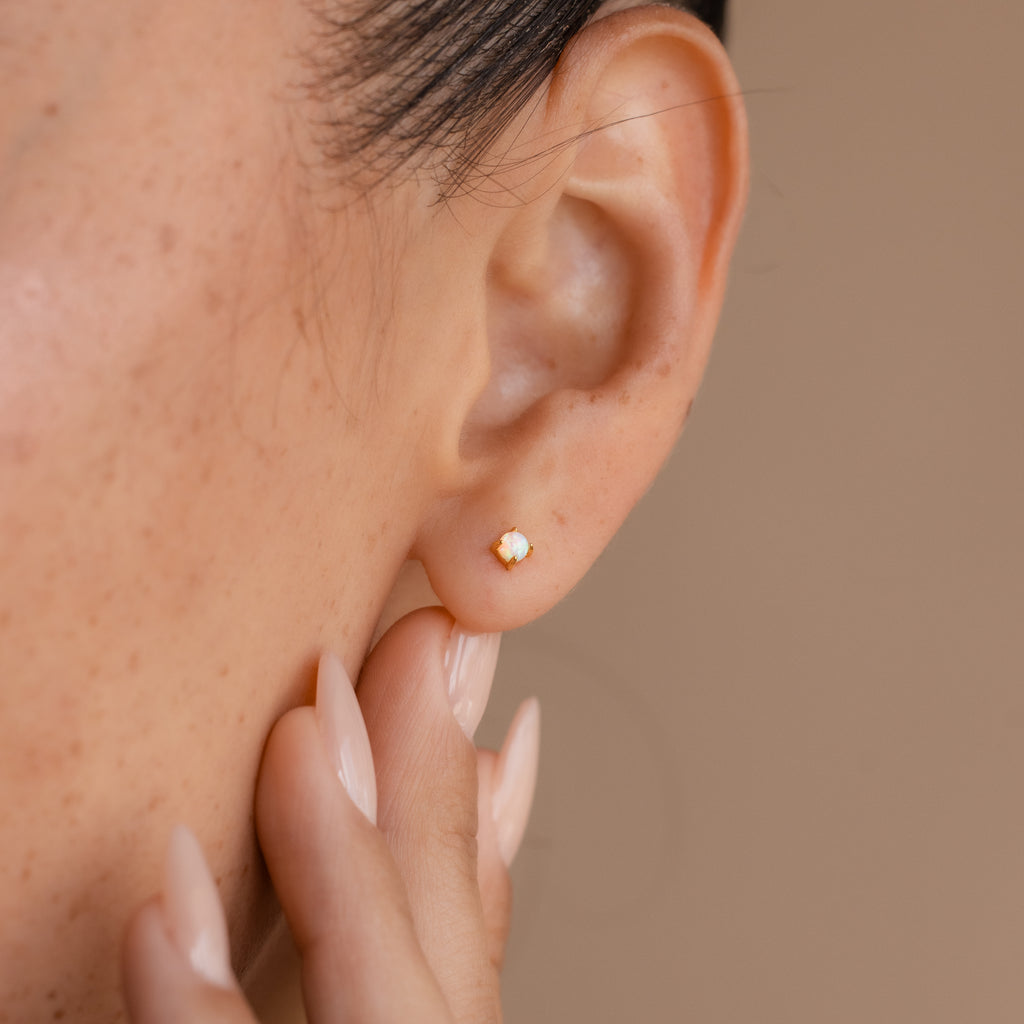 Close-up of an ear wearing the Opal Flat Back Studs in 18K Gold, with a hand gently touching the earlobe to showcase the beauty of these dainty earrings.