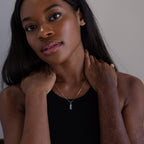 A woman in a black top touches her neck while wearing the Dainty Tag Name Necklace in Sterling Silver, featuring a rectangular pendant on delicate chains.
