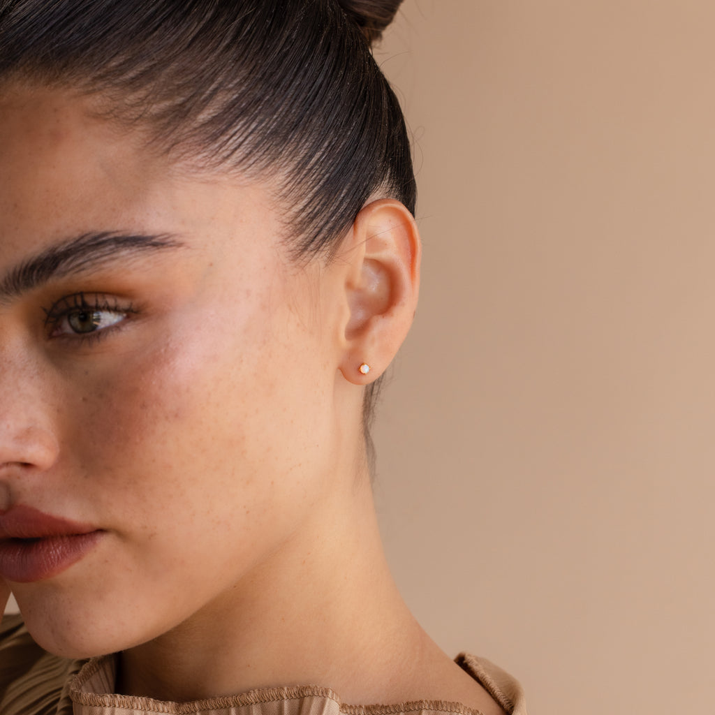 A woman with freckles and a hair bun wears dainty Opal Flat Back Studs, adding subtle sparkle to her look.