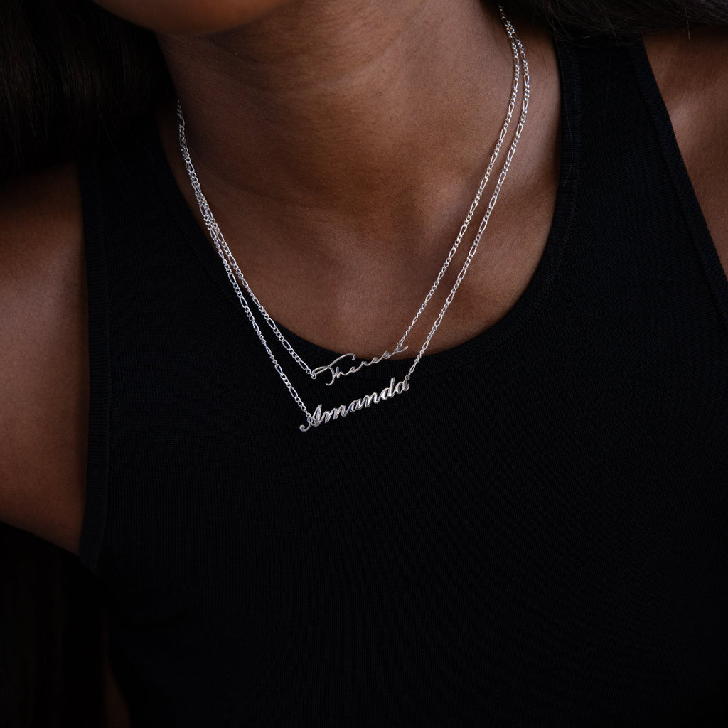 Two silver name necklaces on a person wearing a black top
