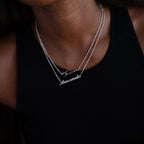 Two silver name necklaces on a person wearing a black top