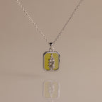 The Peridot Birth Flower Charm Necklace features a rectangular floral pendant on a yellow background, making it an ideal gift for nature lovers and flower jewelry enthusiasts. Displayed on a plain surface.