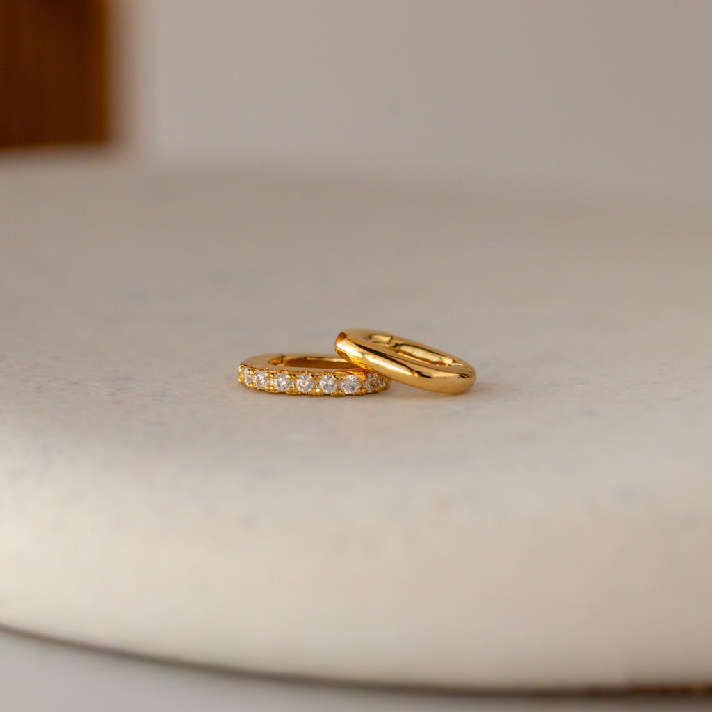 A plain gold ring and a diamond-accented ring sit on a light surface—ideal for personalization or pairing with the Multipurpose Pave Ring Lock Set in 18K Gold.