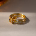 The Multipurpose Pave Ring Lock Set in 18K Gold features three gold rings with diamonds and a heart-shaped gemstone, finished with a pavé-detailed clasp, stacked elegantly on a light surface.