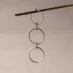 Three silver rings, including the Multipurpose Pave Ring Lock Set in White Gold, hang linked from a twig against a neutral background—highlighting versatile jewelry customization.