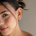 Close-up of a woman with smooth skin, softly smiling while wearing Mini Diamond Sprinkle Huggies in 18K Gold.