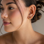 Woman with smooth skin and hair in a bun, wearing Mini Diamond Sprinkle Huggies in 18K Gold, looking to the side.