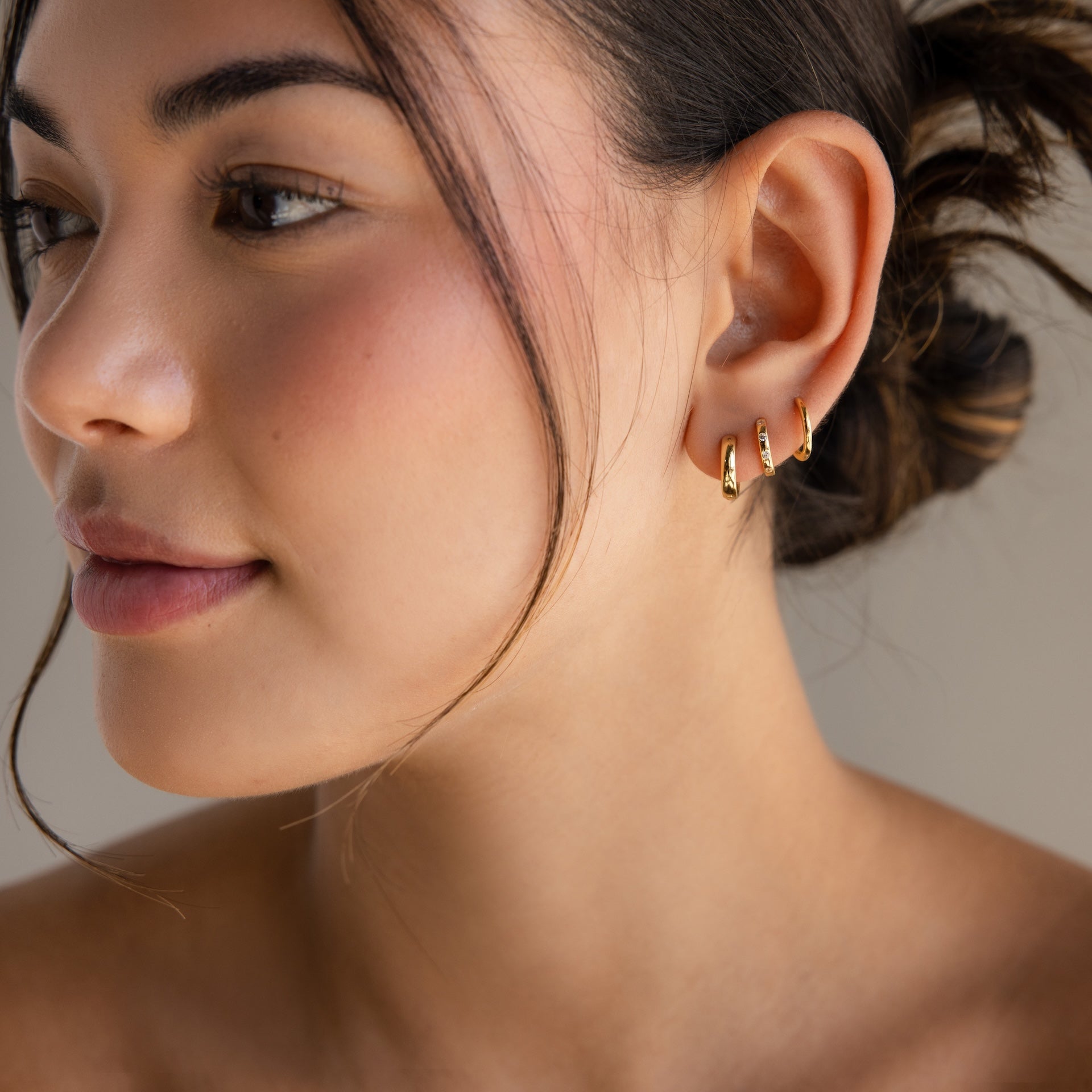Woman with smooth skin and hair in a bun, wearing Mini Diamond Sprinkle Huggies in 18K Gold, looking to the side.