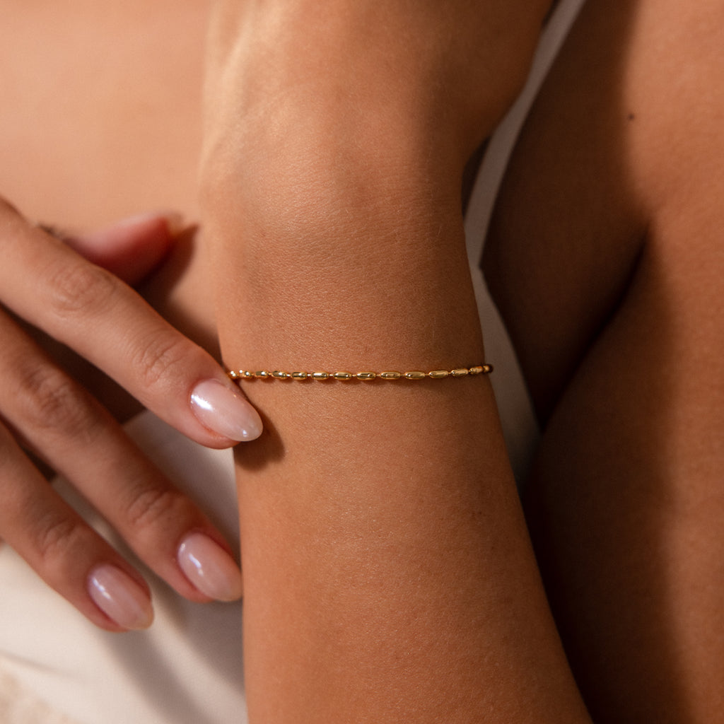 The Oval Beaded Bracelet features polished oval beads, creating a modern classic look when worn on the wrist with manicured hands and a white top.