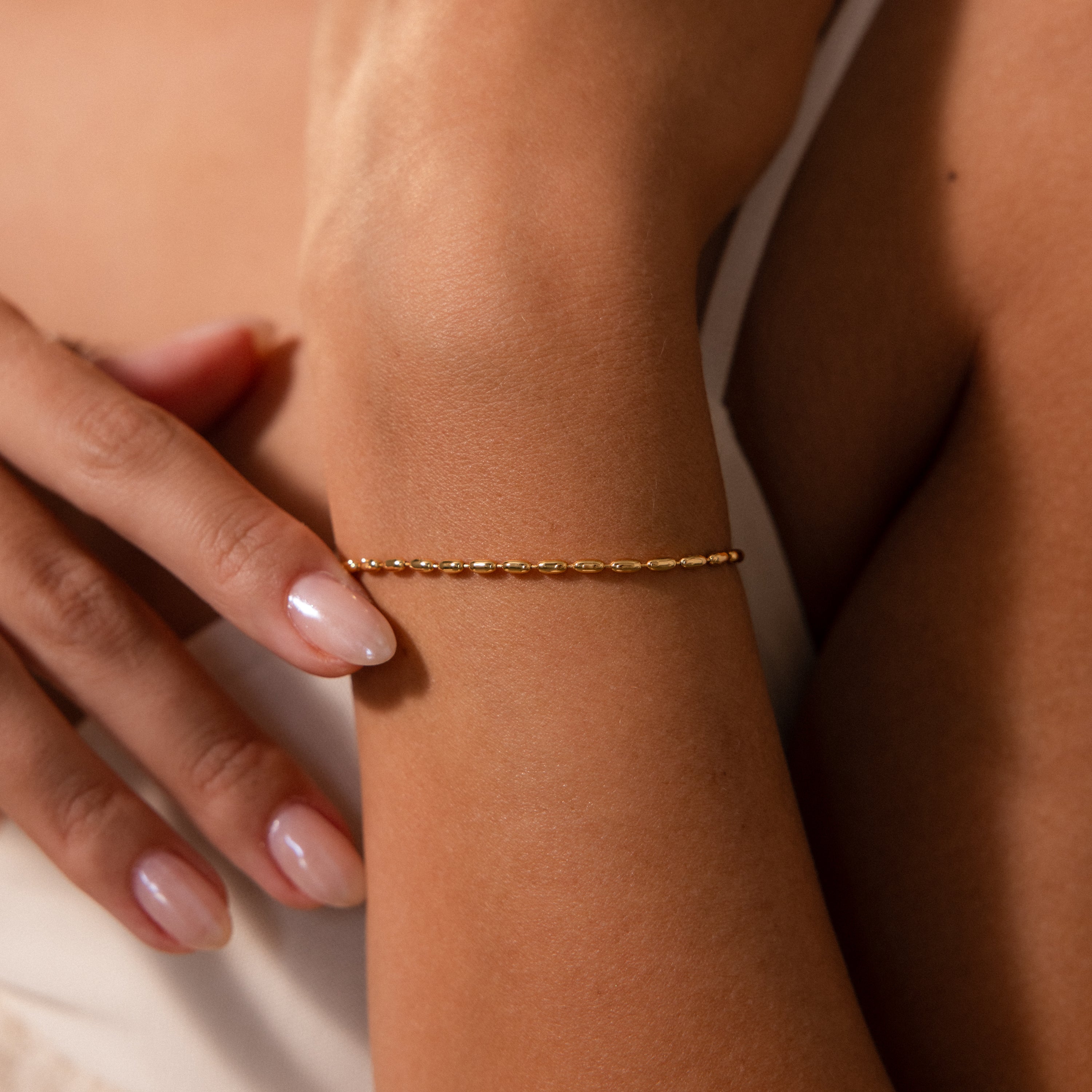 The Oval Beaded Bracelet features polished oval beads, creating a modern classic look when worn on the wrist with manicured hands and a white top.