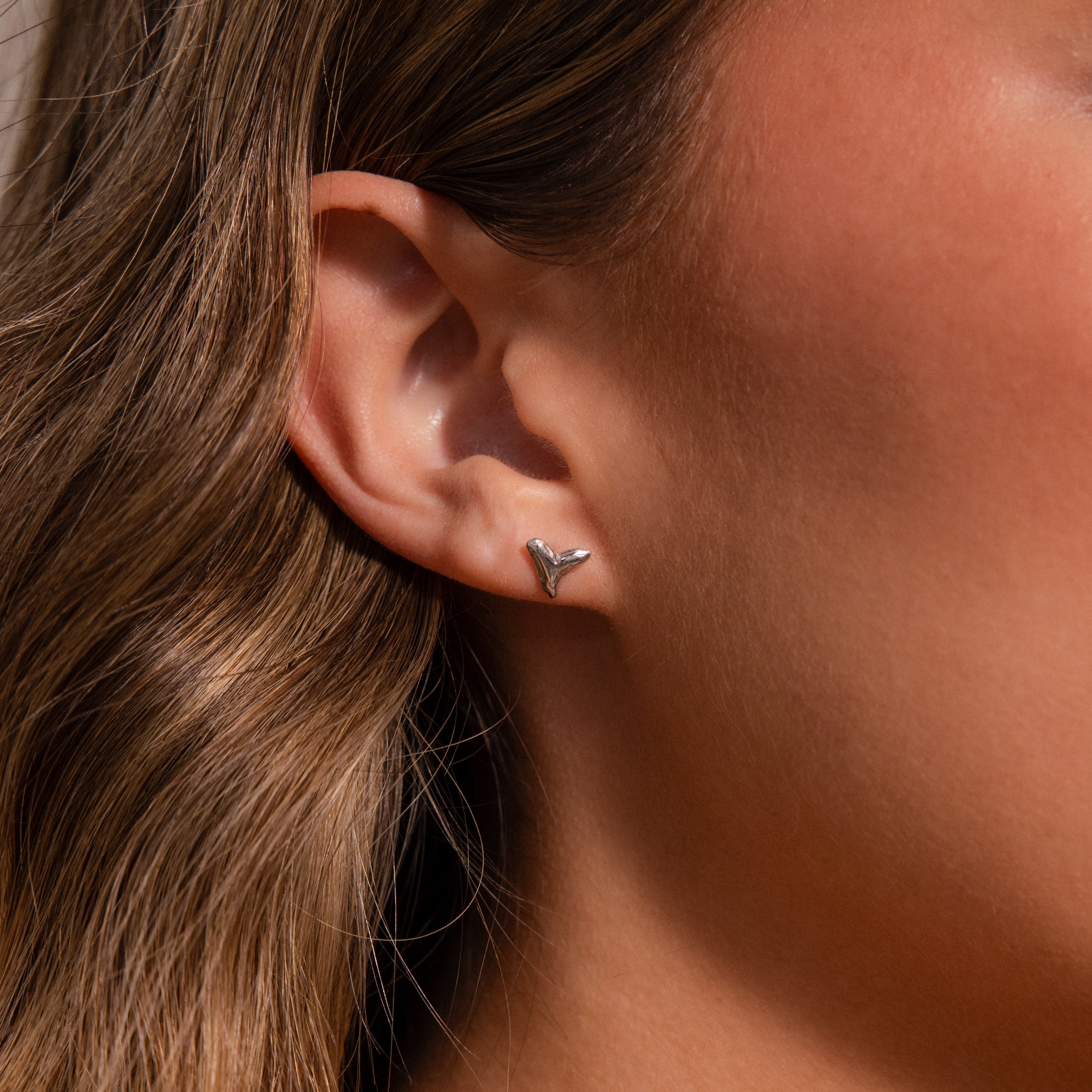 Close-up of a womans ear wearing Shark Tooth Flatback Studs in Silver—a subtle, trendy beach accessory.
