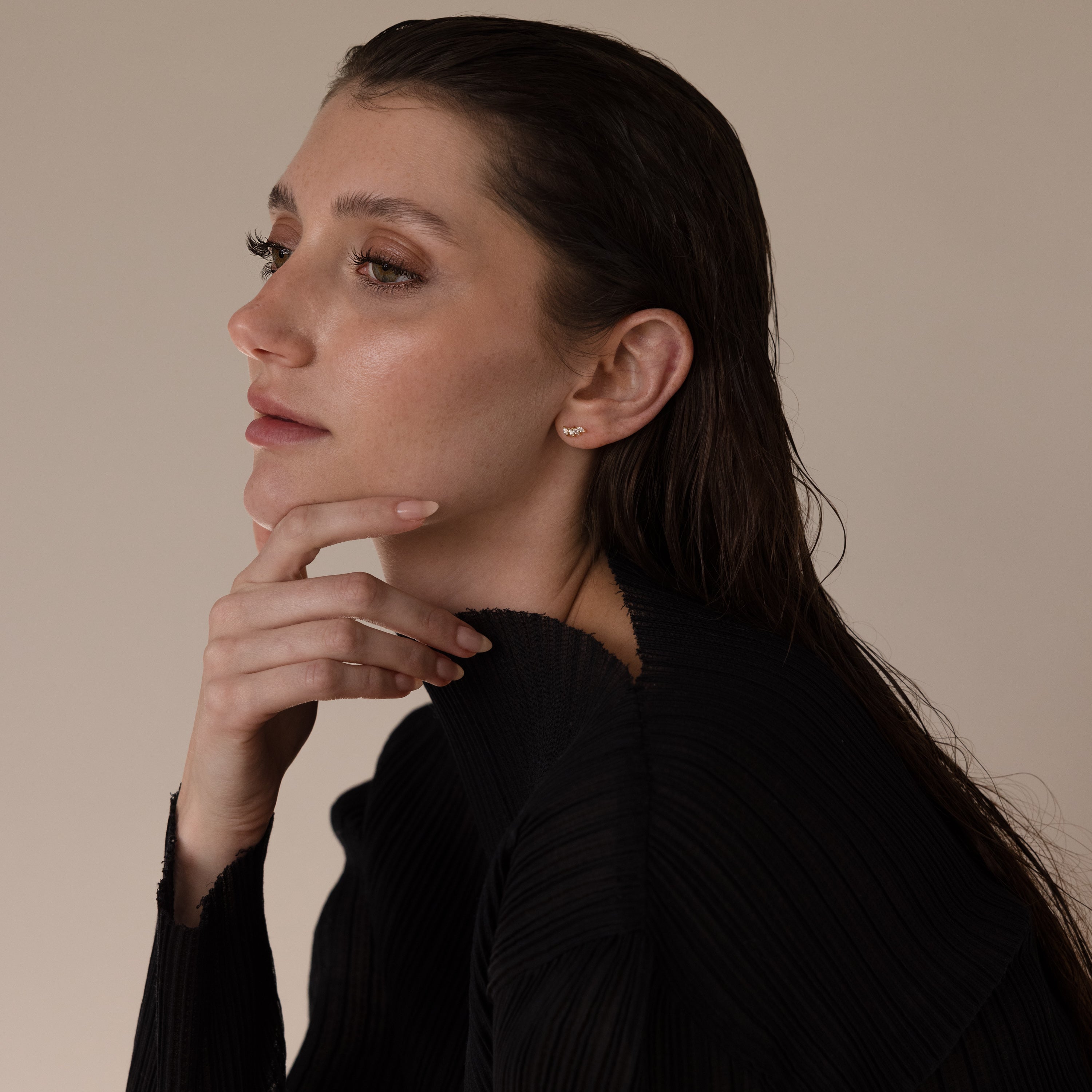 A woman with wet hair in a black top thoughtfully poses, highlighting the Marquise Diamond Climbers earrings against a neutral background.