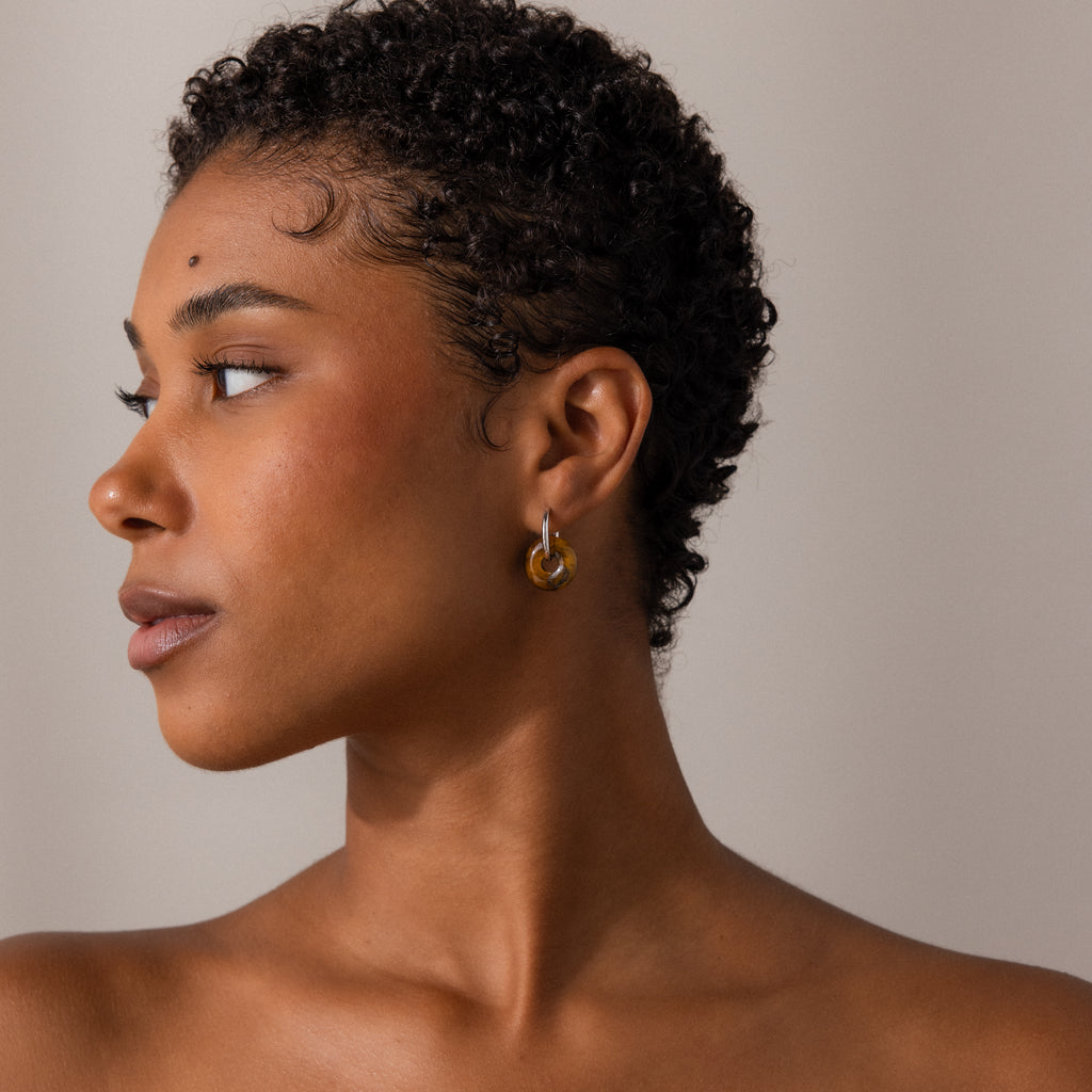 Woman with short curly hair wears the Tiger's Eye Duo Hoops in White Gold, looking to the left against a neutral background.
