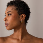 Woman with short curly hair wears the Tiger's Eye Duo Hoops in White Gold, looking to the left against a neutral background.