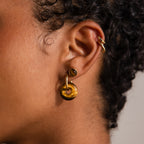 Close-up of an ear with curly hair adorned by Tiger's Eye Duo Hoops in 18K Gold, complemented by a stud and a gold ear cuff.
