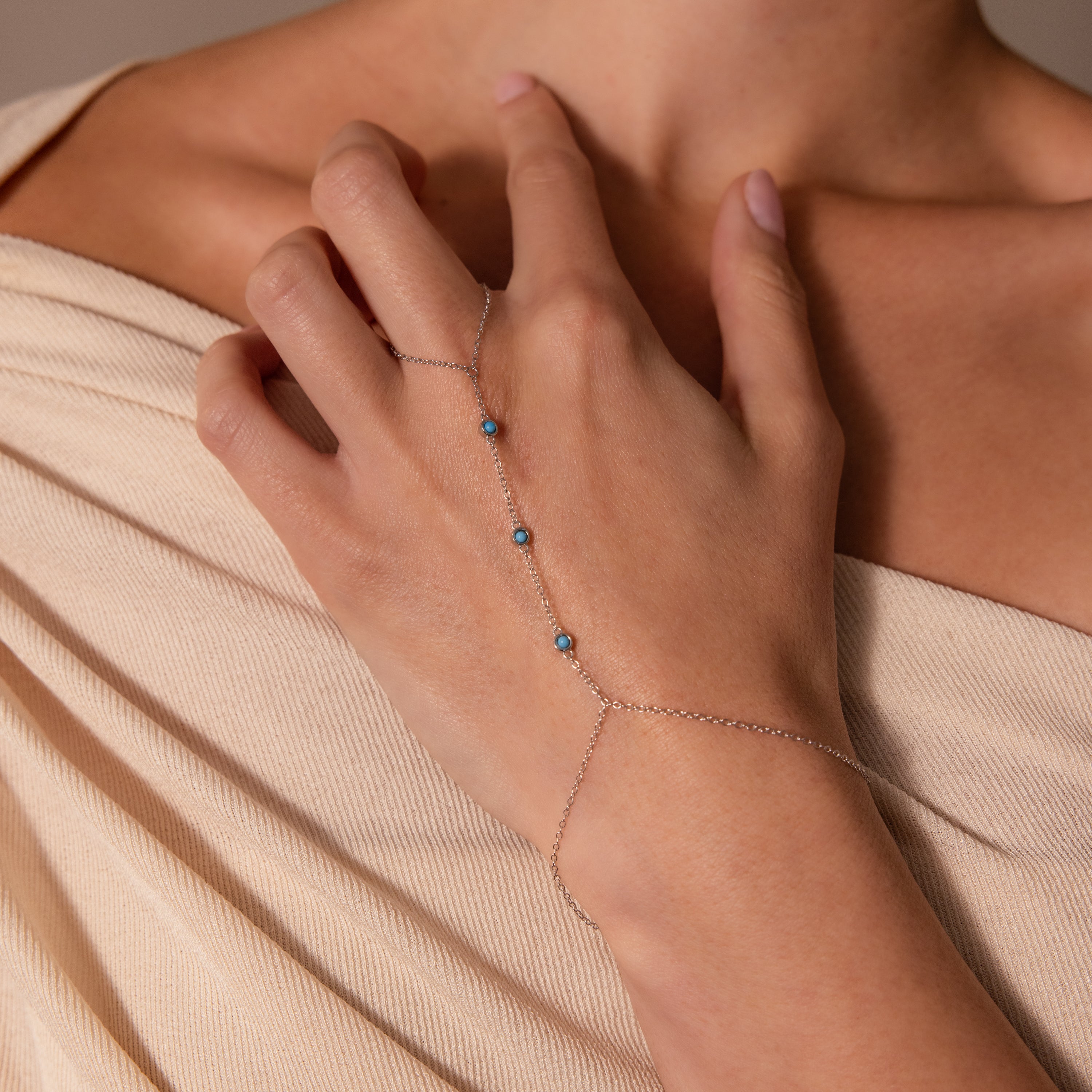 A woman wears the Turquoise Hand Chain Bracelet with blue beads over beige, off-shoulder fabric.