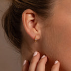 Close-up of a womans ear wearing Floating Pink Tourmaline Huggies, with her hand near her neck.